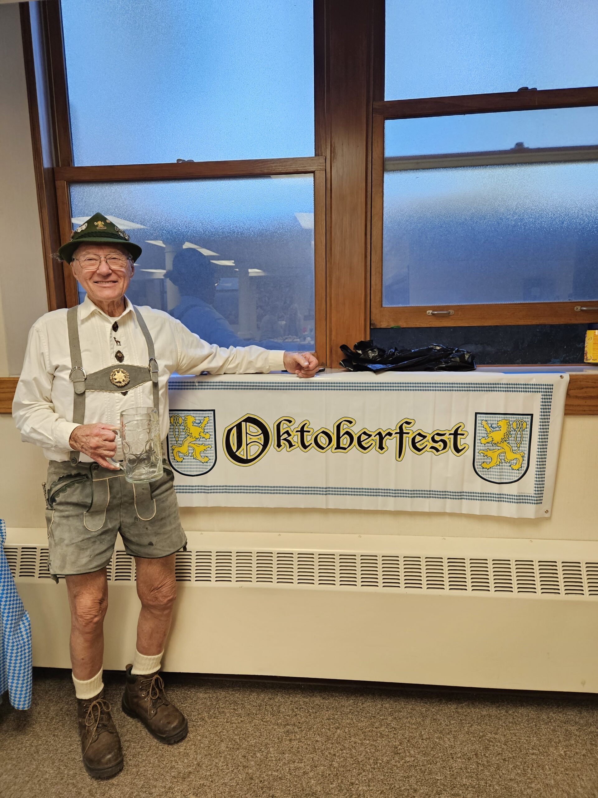 Man wearing lederhosen in front of Oktoberfest banner at Bethlehem Lutheran Church in West Dundee, IL